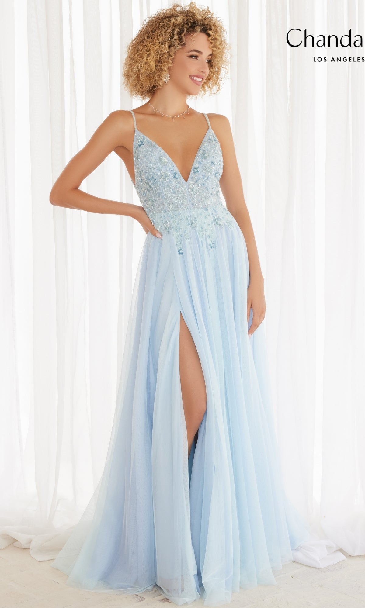 A woman in the Long Prom Dress 30165 by Chandalier, featuring a light blue A-line silhouette, thin straps, deep v-neckline, floral embroidery, and a high slit, stands against a white background.